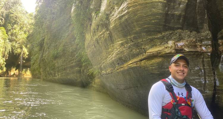Persona sonriendo con un chaleco de seguridad junto a un río rocoso.