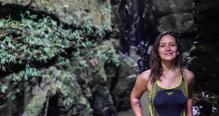 Persona de pie frente a exuberantes cascadas y rocas.