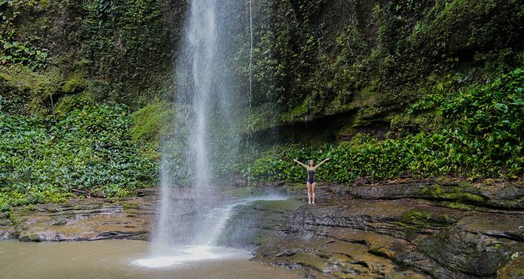 Persona con los brazos extendidos de pie frente a una cascada.