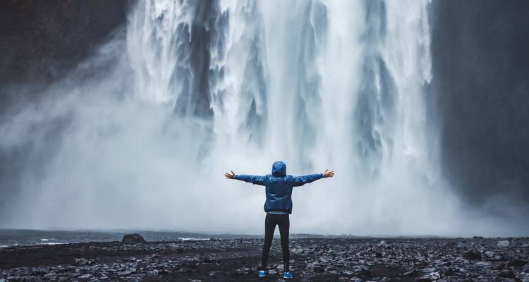 Person standing with arms outstretched in front of a massive waterfall.
