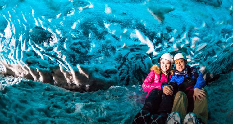 Two people in a colorful ice cave, wearing helmets.