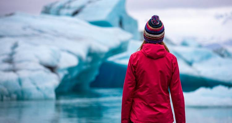 Person in a red coat standing in front of large ice formations.