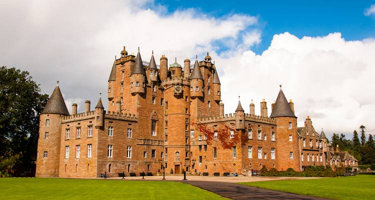 Impressive red-sandstone Glamis Castle surrounded by manicured lawns under blue skies