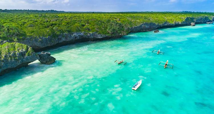 Türkisfarbenes Wasser mit Booten entlang einer zerklüfteten Küstenlinie.