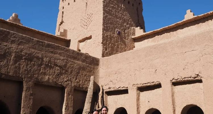 Zwei Personen stehen vor Lehmziegelarchitektur, möglicherweise in einer Kasbah.