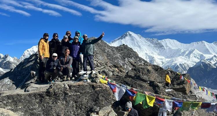 Group of trekkers posing in front of snowy peaks with prayer flags.