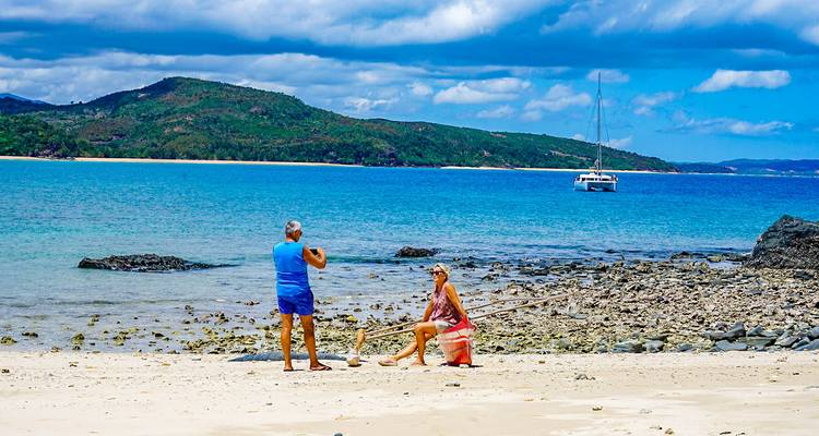 Zwei Personen an einem Strand mit einem Katamaran im Hintergrund.