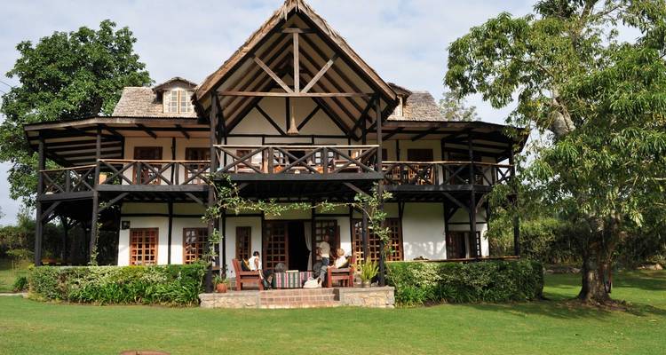 Haus im Kolonialstil mit einem Balkon und Leuten, die auf der Veranda sitzen.