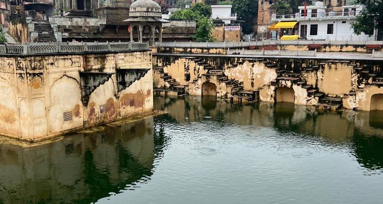Historischer Stufenbrunnen oder Wassertank mit gewölbten Nischen und verwitterten ockerfarbenen Mauern, die sich in grünem Wasser spiegeln.