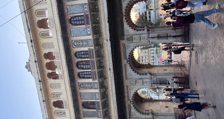 Großes dreibogiges Tor eines kunstvollen Havelis mit Blick auf einen Ghat am Seeufer, mit Besuchern, die unter den geschnitzten Balkonen wandeln.