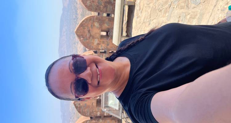 Selfie einer Frau auf einer Sandsteinburg-Terrasse mit Blick auf trockene Hügel und Festungswälle unter einem klaren blauen Himmel.