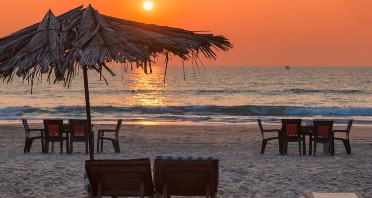 Strandszene mit Sonnenuntergang, Sonnenschirmen und Liegestühlen.