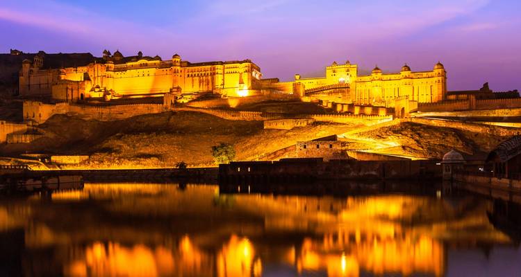 Amber Fort wunderschön beleuchtet bei Sonnenuntergang mit Spiegelungen im Wasser.
