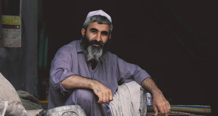 Porträt eines Mannes mit Bart, der in einem schwach beleuchteten Raum sitzt.