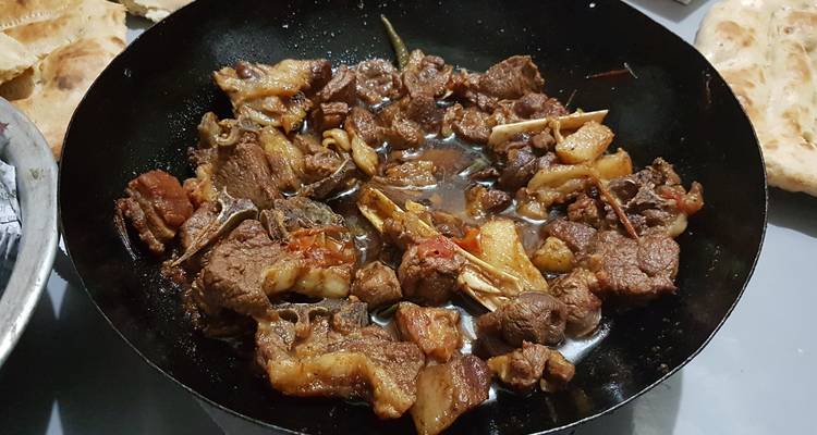 Traditionelles Gericht mit Fleisch, das in einer großen Pfanne zubereitet wird.