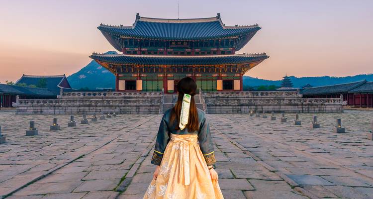 Person in traditional dress facing an ornate historical building at twilight.
