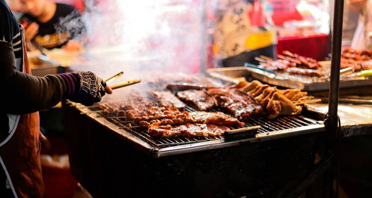 Barbecue with various meats grilling at a night market.