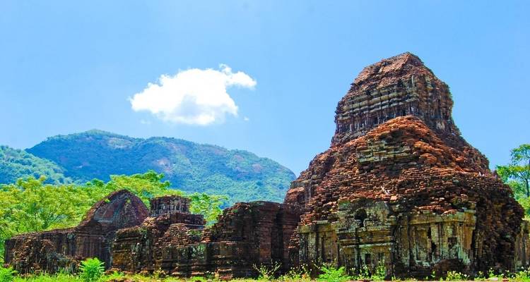 Oude bakstenen tempels omringd door weelderig groen en bergen onder een heldere blauwe hemel.