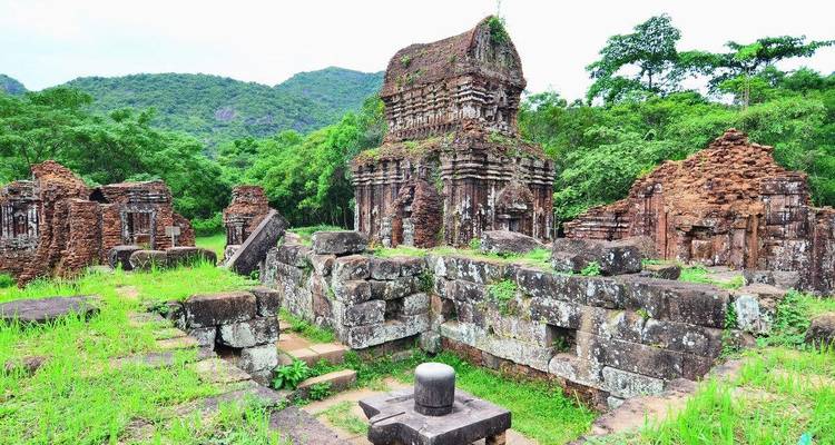 Ruïnes van oude tempels te midden van groen met bergen in de verte.