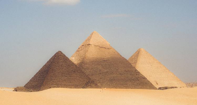 Las tres Grandes Pirámides de Giza elevándose desde las arenas doradas del desierto bajo un cielo brumoso.