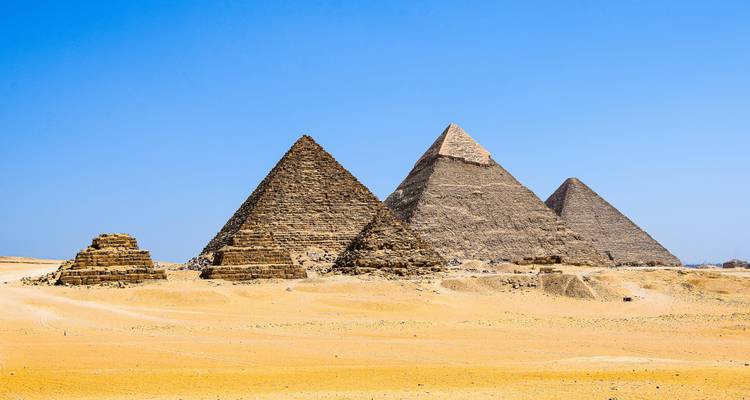 Vista de gran angular del complejo de pirámides de Giza contra un cielo azul brillante y una vasta llanura desértica.