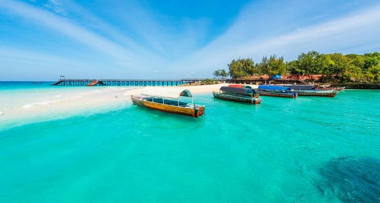 Türkisfarbenes Wasser mit traditionellen Holzbooten in der Nähe eines Sandstrandes.