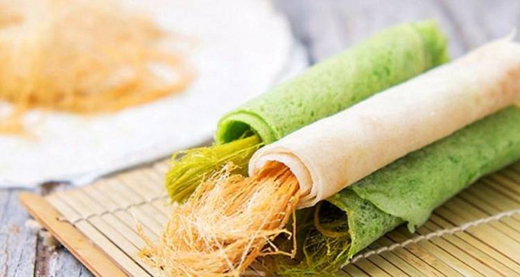 Traditional Thai dessert with green and white rolls on bamboo mat.