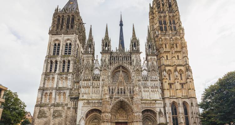 Gotische Fassade der Kathedrale von Rouen mit kunstvollen Türmchen und aufragenden Türmen vor einem bewölkten Himmel.
