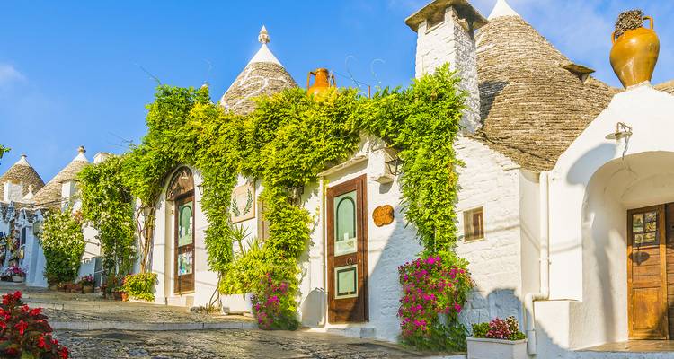 Zonovergoten laan omzoomd met witgekalkte trulli-huizen behangen met groene ranken en bloemen