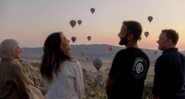 Grupo de personas observando globos aerostáticos en el cielo.