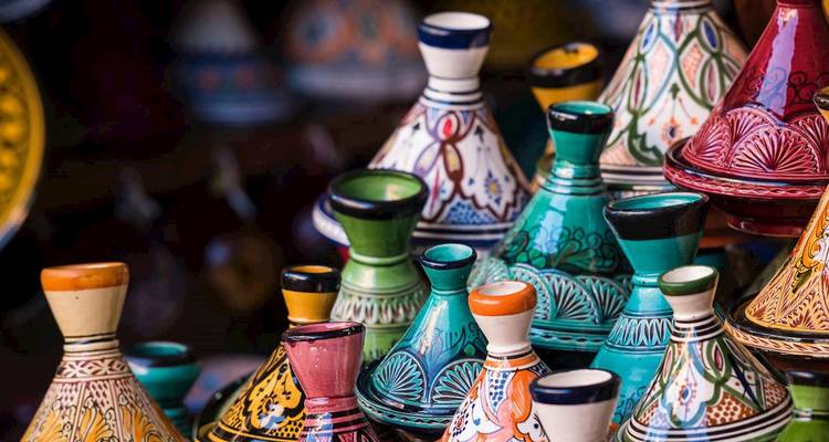 Tajines en céramique marocaine peints à la main et colorés empilés dans un étal de marché animé.