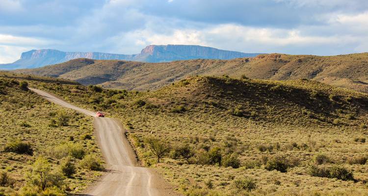 Zandweg die door een heuvelachtig, ruw landschap snijdt.