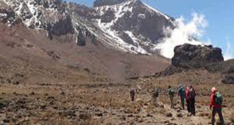 Des randonneurs se déplaçant à travers un paysage accidenté avec des sommets enneigés.