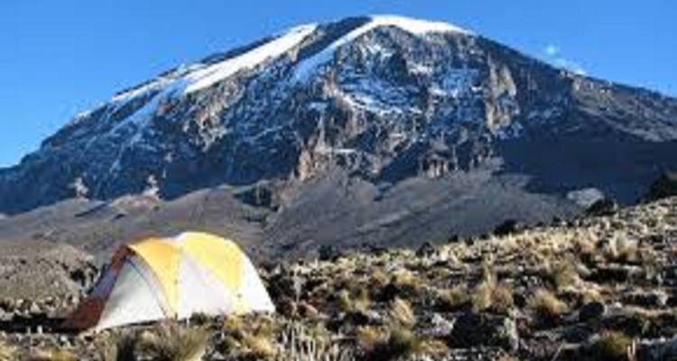Une tente installée au pied d'une grande montagne, montrant le camping dans un lieu pittoresque.