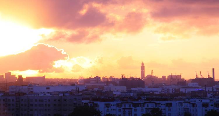 Vibrant sunset over Casablanca skyline with silhouette of Hassan II Mosque tower and golden clouds.