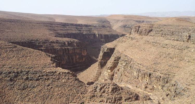 Paysage aride de canyon rocheux avec des falaises stratifiées et des plateaux sous un ciel brumeux.