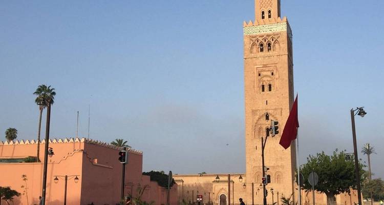 Le haut minaret de la mosquée de la Koutoubia s'élève au-dessus des rues bordées de palmiers et d'un drapeau marocain à Marrakech.