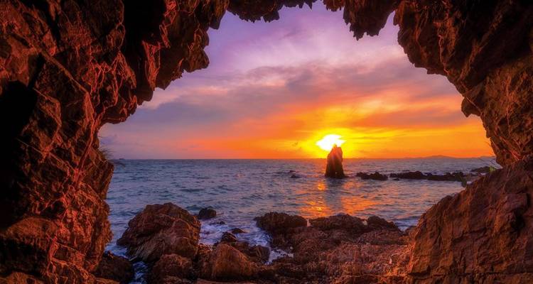 Vue du coucher de soleil à travers une grotte rocheuse le long d'une zone côtière.