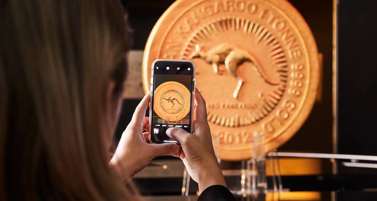 Persona tomando una foto de una exhibición de una gran moneda de oro