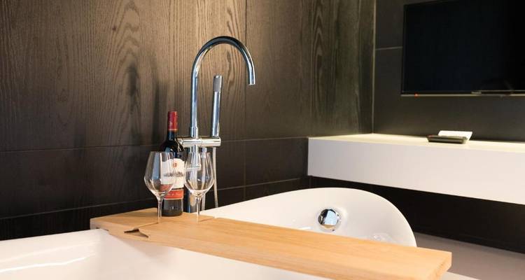 Salle de bain de luxe avec des équipements modernes et du vin sur une étagère de baignoire.
