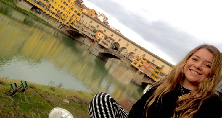 Person smiling with the Ponte Vecchio bridge in Florence visible in the background.