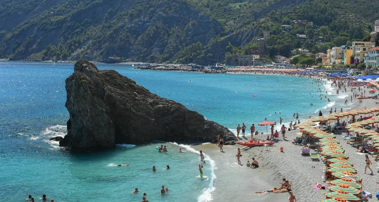 Scenic beach with a large rocky outcrop and numerous visitors by the shore.