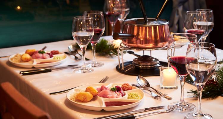 Eleganter Esstisch, eingedeckt für Käsefondue mit Weingläsern, Kerzenlicht und ordentlich angerichteten Tellern.