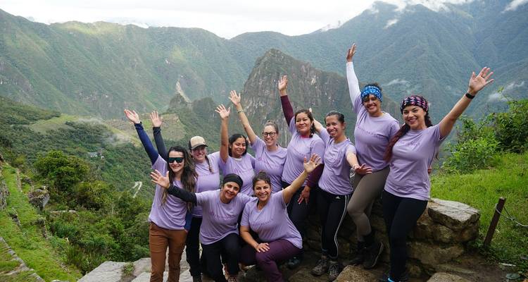 Groep vrouwen poserend met armen omhoog voor Machu Picchu.