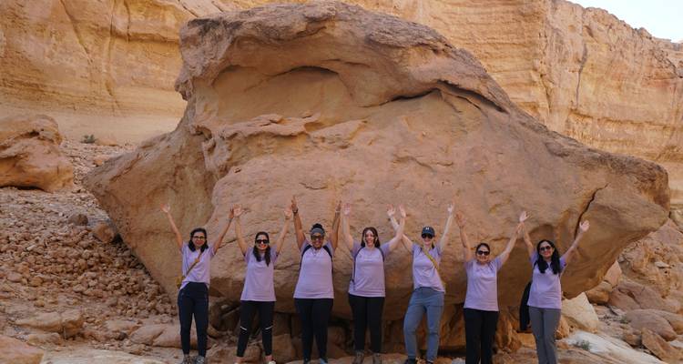 Groupe de femmes posant avec les mains levées devant une grande formation rocheuse.