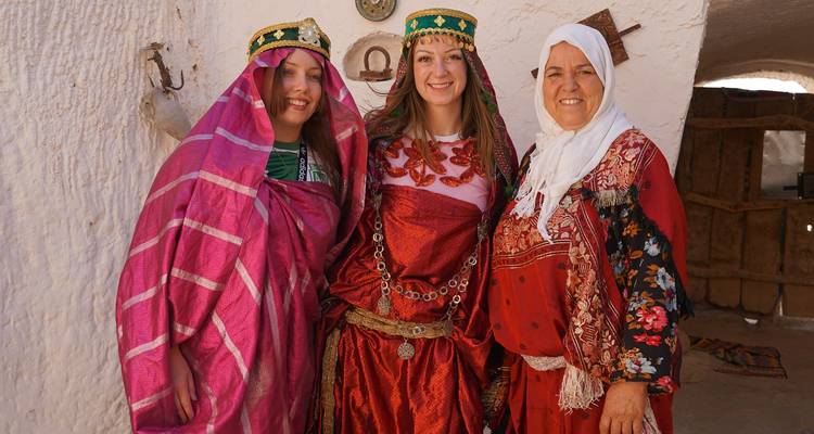 Trois femmes en tenue traditionnelle posant à l'intérieur d'une maison en argile.