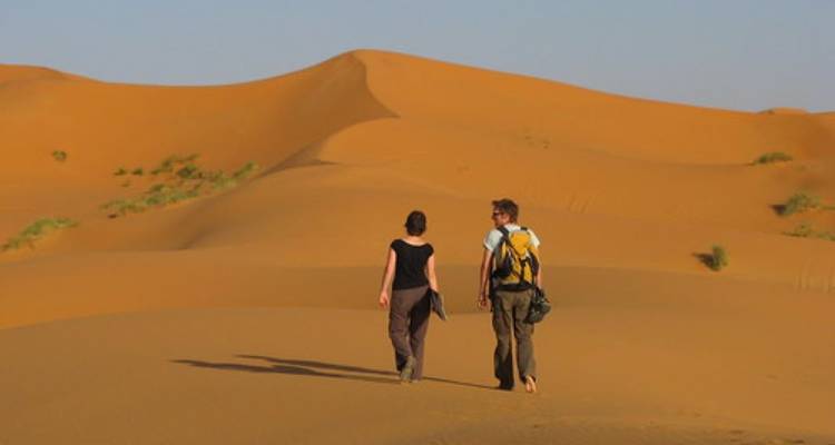 Zwei Menschen, die über Sanddünen gehen.