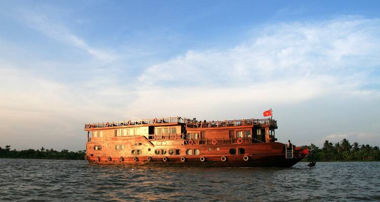 Elegant wooden cruise vessel sailing on a calm river at sunset.