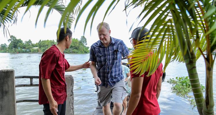 Local guides assist a tourist stepping from a dock beside tropical foliage.