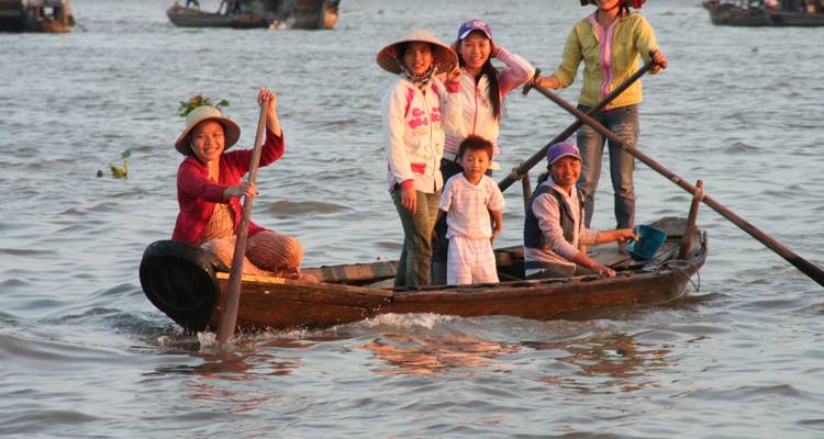 Smiling family rowing a small wooden boat on a busy river.